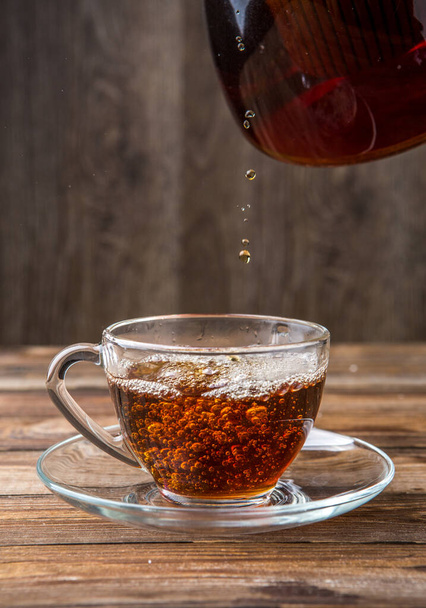 Çaydanlıktan dökülen bitkisel çay fincanda kahverengi ahşap masa - Fotoğraf, Görsel
