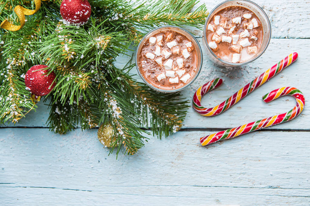 Two glasses of cocoa with marshmallows and christmas tree with toys on white wooden background. View from above - Photo, Image