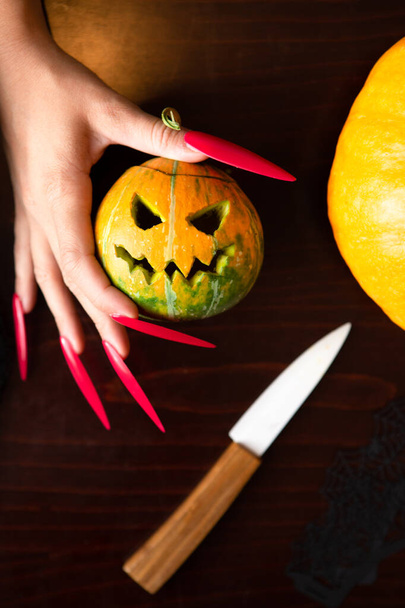 Image of woman's hands with pink nails with pumpkin jack, spider, knife sitting at wooden table in halloween - Photo, Image