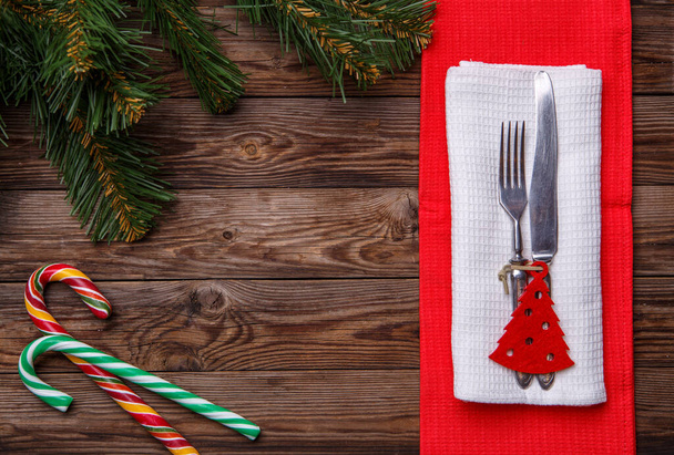 Çatal ve bıçakla hazırlanmış Noel masası, süslü Noel oyuncağı - kırmızı köknar ağacı, iki lolipop kamışı ve noel çamı dalları. Noel tatili geçmişi. - Fotoğraf, Görsel