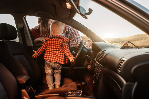 Šťastná mladá rodina maminka a tatínek s jejich syn malý řidič těší letní víkend piknik na autě mimo město na poli při slunečném dni západ slunce, dovolená a silniční výlet koncepce - Fotografie, Obrázek