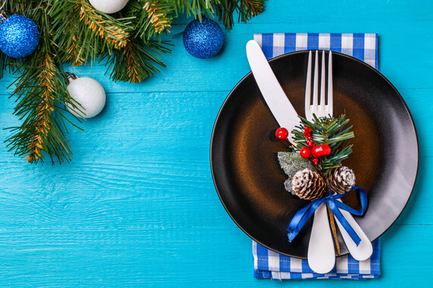 Kerst tafelschikking met servet, zwarte plaat, witte vork en mes, versierde takje maretak en kerst dennen takken. Kerstvakantie achtergrond. - Foto, afbeelding