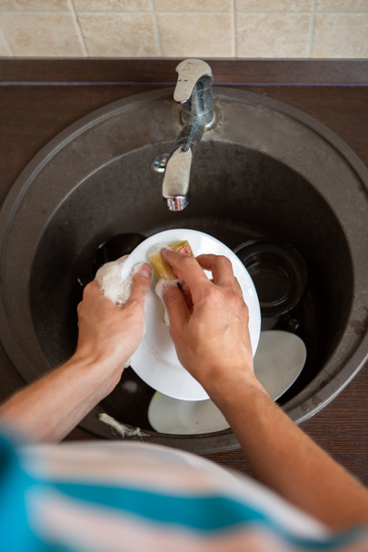 Image from above of man's hands washing the dish into sink in kitchen - Photo, Image