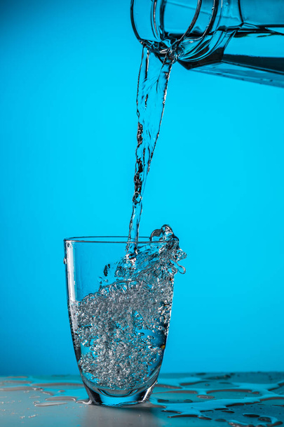 Ember önti a vizet az üvegből az üvegbe a kék háttér stúdióban - Fotó, kép