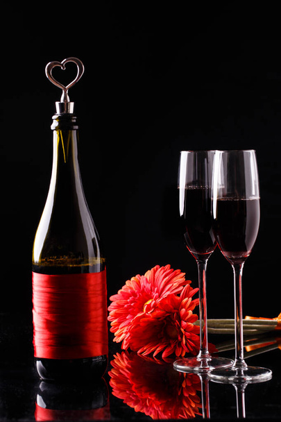 Butelka, kwiat, kieliszki do wina na stole na czarnym tle - Zdjęcie, obraz