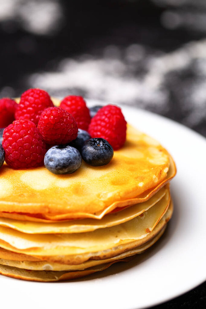Closeup photo of plate of pancakes, blueberries, raspberries and powdered sugar on black table - Фото, зображення