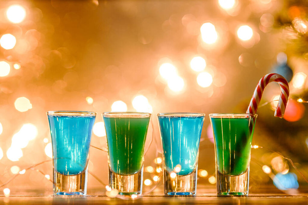 Vánoční obrázek čtyř sklenic na víno se zeleným koktejlem, karamelovými tyčinkami a věncem na rozmazaném modrém Novém roce - Fotografie, Obrázek