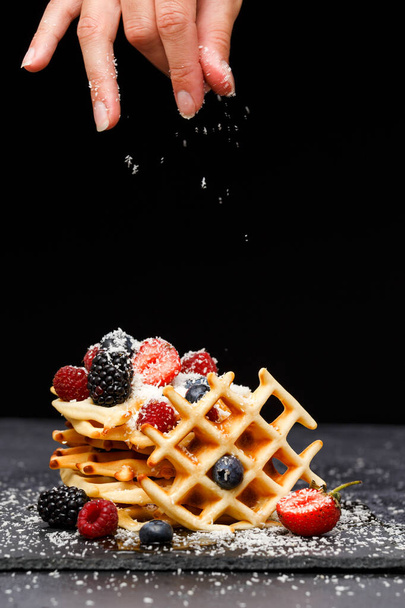 Photo of viennese wafers with raspberries, strawberries sprinkled with powdered sugar on blackboard against blank background in studio - Photo, Image