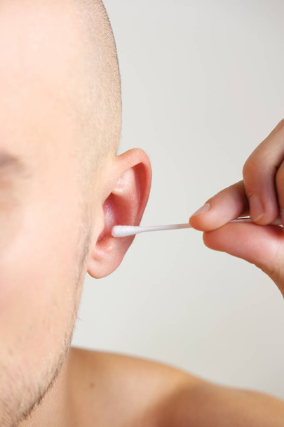 Young man cleans his ears with a cotton swab, close up view. - 写真・画像