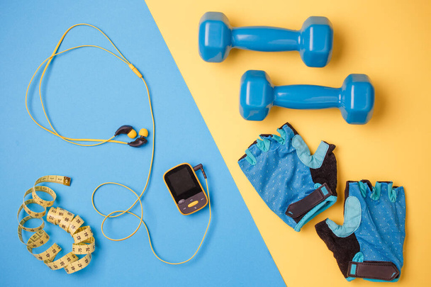 Foto van onderwerpen van fitness. Speler, halters, fles water, centimeter tape, handschoenen op blauwe en gele achtergrond - Foto, afbeelding