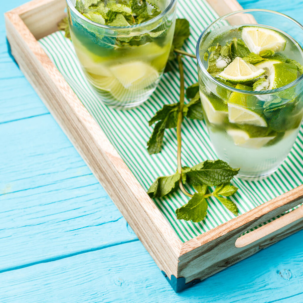 Two glasses of mojito in wooden box with mint on blue wooden table - 写真・画像