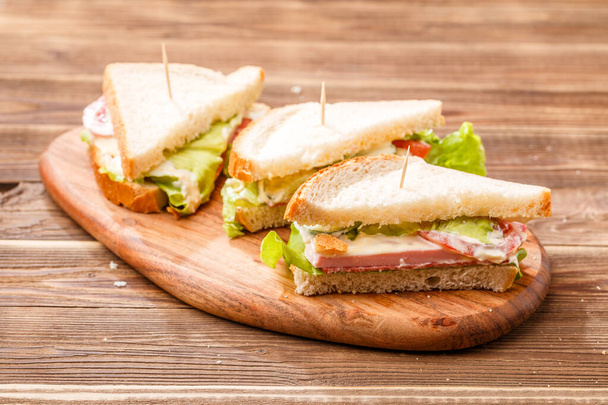 Image of sandwiches with toothpicks and fresh vegetables on wooden board - 写真・画像