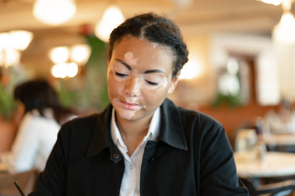 Una hermosa joven de etnia africana con vitiligo sentado en un restaurante
 - Foto, imagen