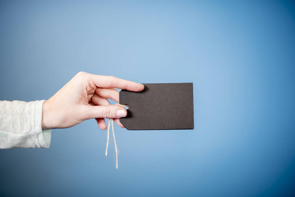A closeup shot of a female holding a blank black tag with a blue background - great for witting text - Φωτογραφία, εικόνα