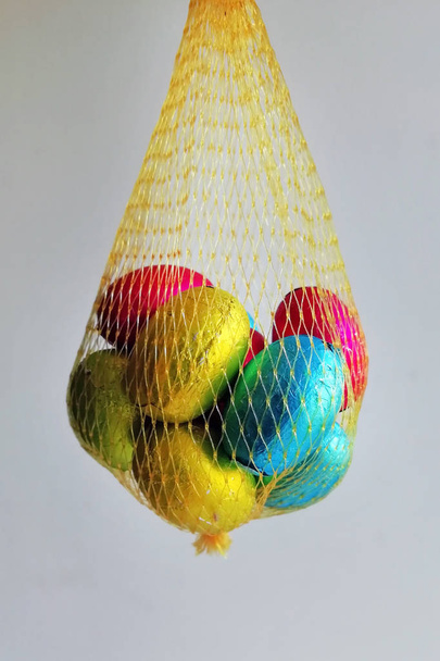 Huevos multicolores envueltos en papel de aluminio doblado en una malla amarilla. Huevos de chocolate en una bolsa para niños
. - Foto, imagen