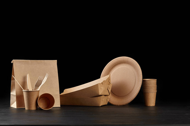 Eco friendly disposable tableware standing on dark surface against black background. Biodegradable craft dishes. Recycling concept. Close-up shot. - Φωτογραφία, εικόνα