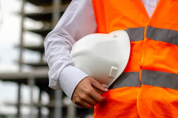 Trabajador con casco de seguridad blanco y chaleco naranja. Concepto de trabajadores de la construcción e industriales
 - Foto, Imagen