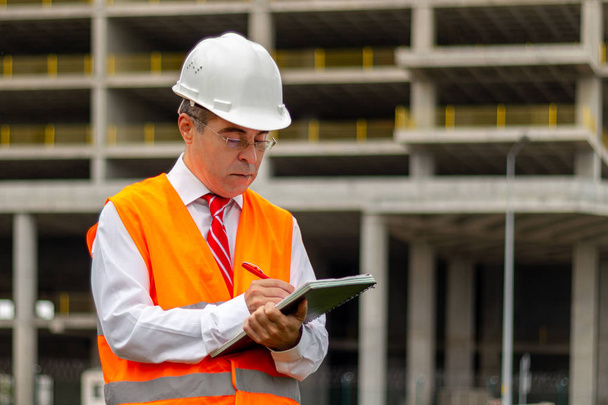 Építőmérnök férfi ingben és nyakkendőben, biztonsági sisakkal és mellénnyel az építkezésen. Az ipari területen dolgozó emberek fogalma - Fotó, kép