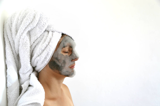 Young woman with a black bubble charcoal oxygen mask on her face and towel on the head. Beauty spa acne treatment. Popular face mask. - 写真・画像