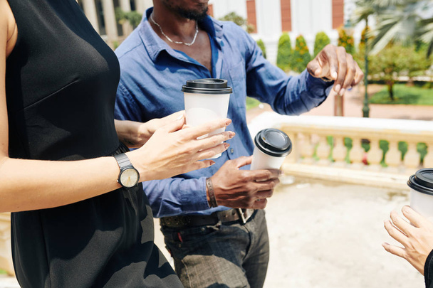 geschnittenes Bild von Geschäftsleuten mit Kaffee zum Mitnehmen, die an sonnigen Tagen auf der Straße spazieren und Neuigkeiten und Ideen diskutieren - Foto, Bild