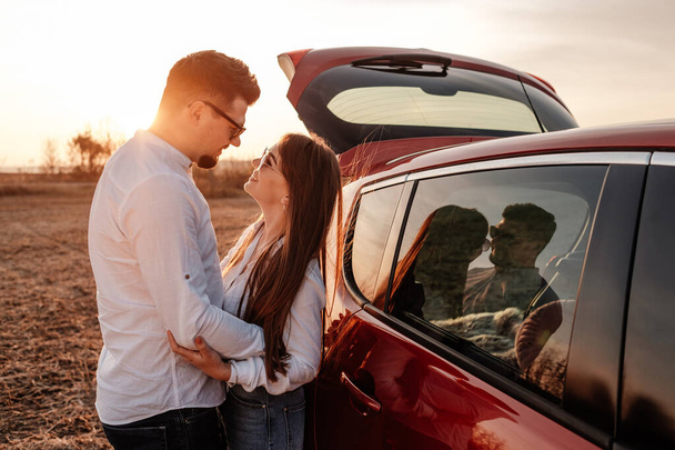 Młoda szczęśliwa para ubrana jak w białej koszuli i dżinsach korzystających z podróży drogowej w ich nowym samochodzie, piękny zachód słońca na polu, wakacje i podróży Concept - Zdjęcie, obraz