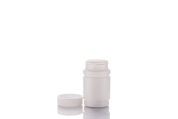 A jar of pills and an open lid stands on a mirror surface on a white background in the middle. - Photo, Image