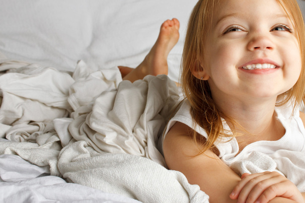 Sorridente giovane ragazza nel letto bianco coperto
 - Foto, immagini