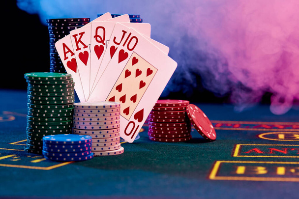 Výherní kombinace v pokeru opírající se o barevné žetony na modrém krytu hracího stolu. Černá, kouřové pozadí, červená a modrá podsvícení. Kasino. - Fotografie, Obrázek