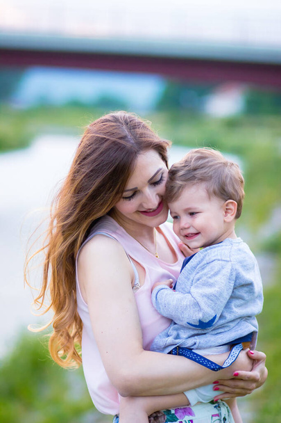 Young mom holding her beautiful blond son, looking at him with love - Фото, зображення