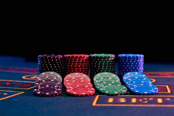 Colorful chips nicely laid out near piles on blue cover of playing table. Black background. Gambling entertainment, poker, casino concept. Close-up. - Photo, Image