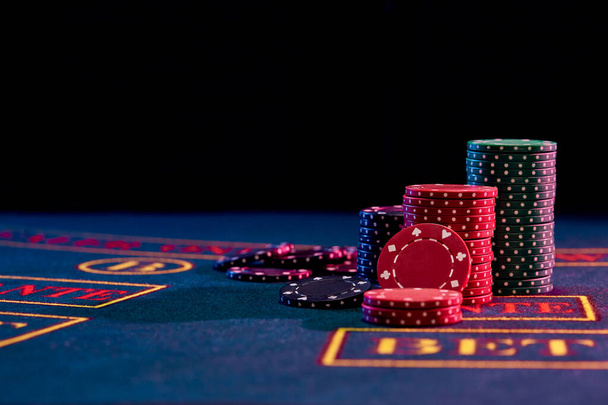 Barevné žetony stojící na modrém obalu hracího stolu. Černé pozadí. Hazardní hry, poker, kasino koncept. Detailní záběr. - Fotografie, Obrázek
