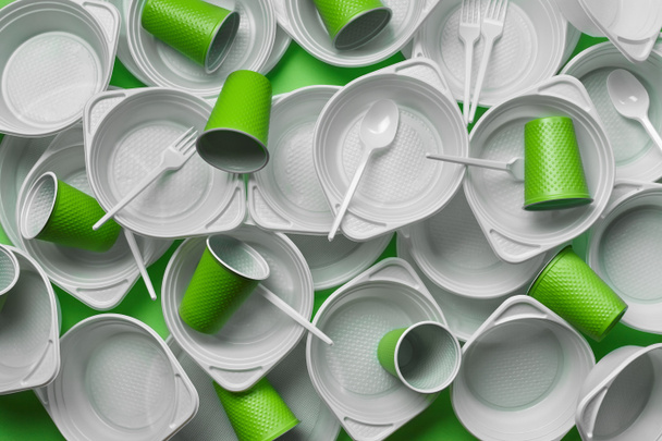 White plastic disposable tableware on green background with copy space. The concept of picnic utensil. Top view. Selective focus. Close-up. - Valokuva, kuva