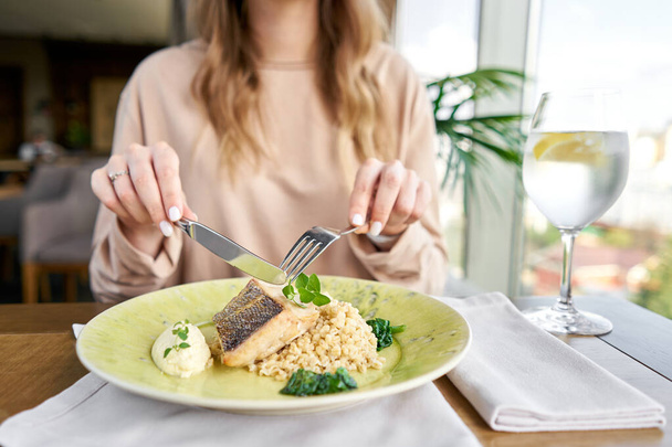 Ψητή πέρκα Πάικ με όλυρα και πολωνική σάλτσα. Γεύμα σε εστιατόριο, μια γυναίκα τρώει νόστιμο και υγιεινό φαγητό. Πιάτα διακοσμημένα με σπανάκι. Μενού εστιατορίου - Φωτογραφία, εικόνα