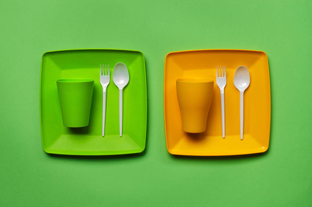Colorful plastic disposable tableware on green background with copy space. The concept of picnic utensil. Top view. Selective focus. Close-up. - Photo, Image