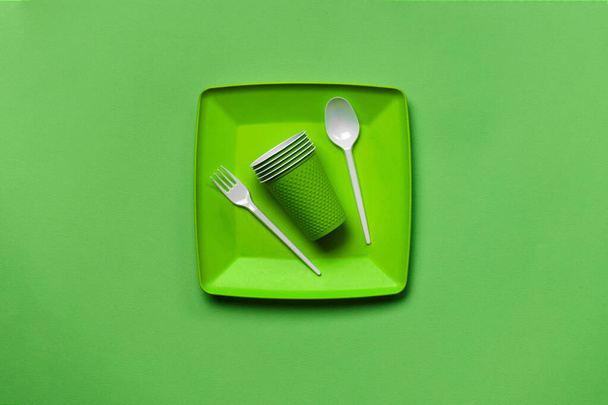 コピースペース付きの緑の背景にカラフルなプラスチック使い捨て食器。ピクニック用品の概念。最上階だ。選択的フォーカス。閉鎖. - 写真・画像