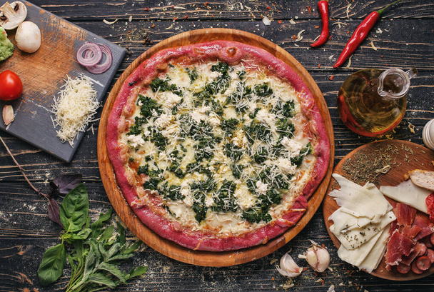 Pizza from black dough with cheese and green on a wooden table. - Photo, Image