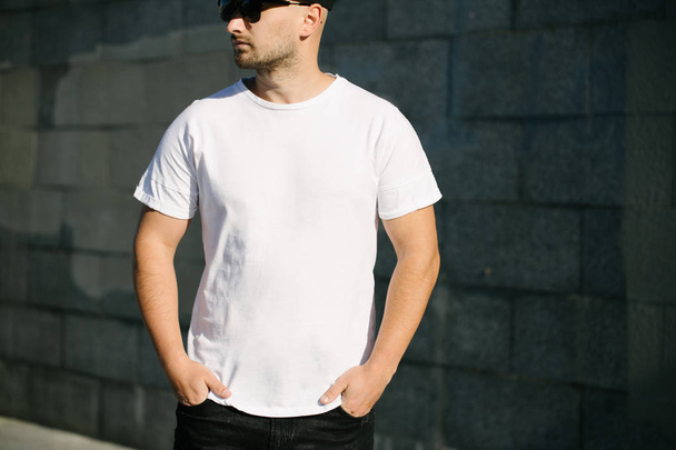 Modelo homem com barba vestindo t-shirt branca em branco e um boné de beisebol com espaço para o seu logotipo ou design em estilo urbano casual
 - Foto, Imagem