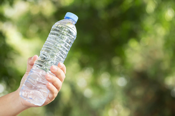 lidé mladá ruka drží čerstvou láhev pitné vody z plastu v parku. - Fotografie, Obrázek