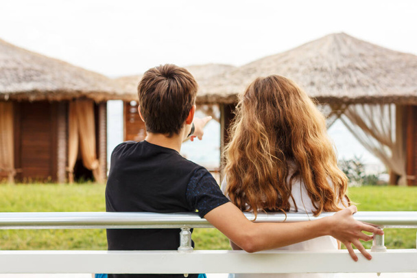 Un par de hermosas adolescentes, primer amor. El tipo abraza a una chica sentada en un banco al lado del otro y mirando al mar
 - Foto, Imagen