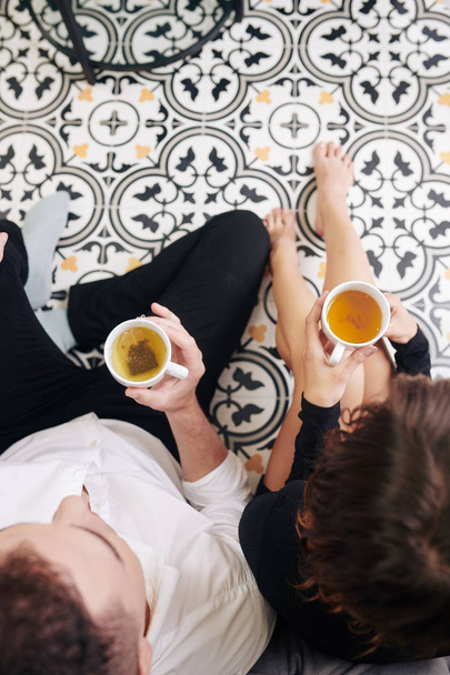 Jong stel zittend op keukenvloer en het drinken van groene thee, uitzicht van boven - Foto, afbeelding