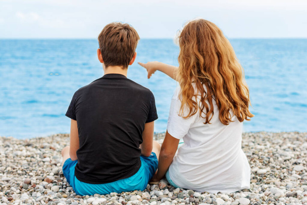 Pari kaunista teiniä, ensirakkaus. Mies halaa tyttöä, joka istuu rannalla vierekkäin ja katselee merta. Ammu takaapäin
 - Valokuva, kuva