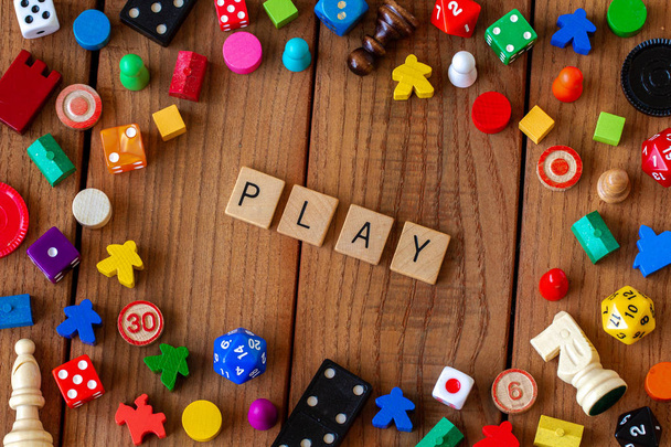 "Play "in hölzernen Buchstabenkacheln geschrieben. umgeben von Würfeln, Karten und anderen Spielsteinen auf einem hölzernen Hintergrund - Foto, Bild