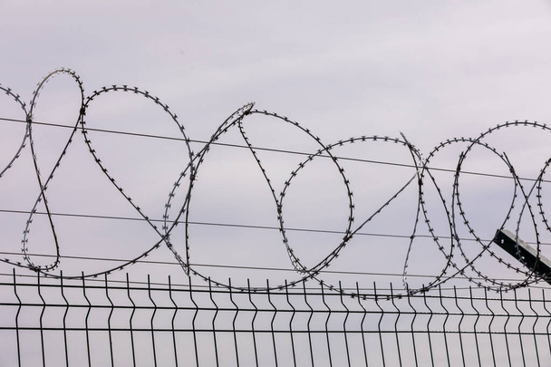 Barbed wire against the cloudy sky. Barbed wire fencing from the prison fence. The concept of captivity, slavery, prisoners, convicted. Prison, checkpoint, security territory, border, military base. - Photo, Image