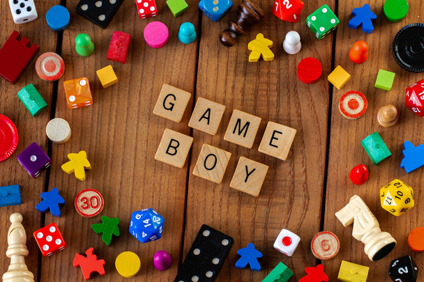 "Game Boy "deletreado en baldosas de madera. Rodeado de dados, cartas y otras piezas del juego sobre un fondo de madera
 - Foto, Imagen