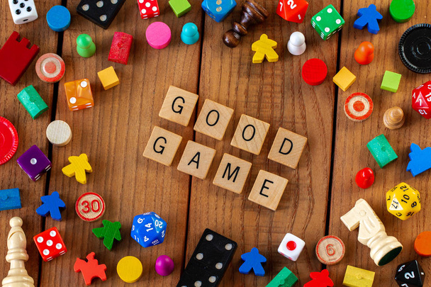 "Dobra gra "zapisane w drewnianych płytkach literowych. Otoczony kości, karty i inne elementy gry na drewnianym tle - Zdjęcie, obraz