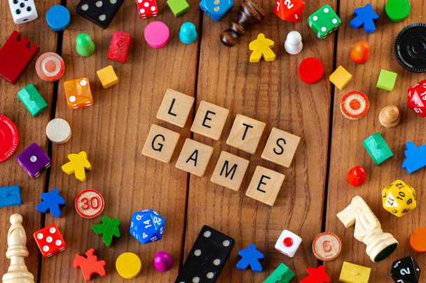 "Lets Game "täsmennetään puinen kirjain laatat. Ympäröivät noppaa, kortit, ja muut pelinappulat puinen tausta
 - Valokuva, kuva