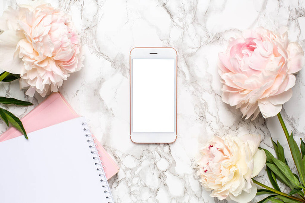Mobile phone with a white and pink notebook and piony flowers on a marble background - Photo, image