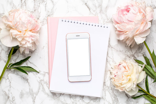 Handy mit weißem und rosa Notizbuch und Pionierblumen auf Marmorhintergrund - Foto, Bild