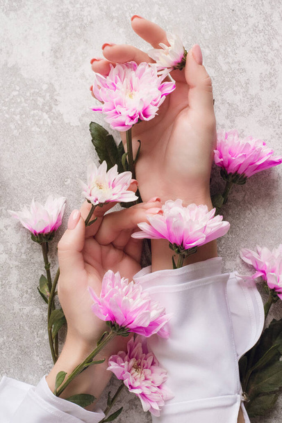 Ręce dziewczyny z delikatnym manicure w kwiatach na szarym tle z różowymi chryzantemami. Koncepcja dbania o skórę dłoni. Kosmetyki naturalne z ekstraktu kwiatowego, piękna i mody - Zdjęcie, obraz