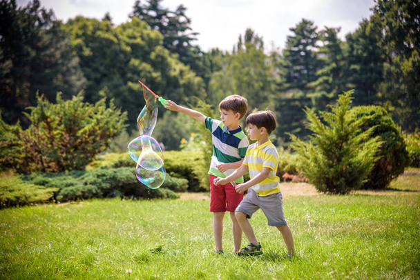 Мальчик надувает мыльные пузыри, в то время как возбужденный ребенок наслаждается пузырьками - Фото, изображение